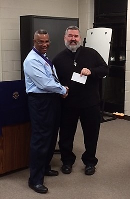 Grand Knight Terry Williams presents a donation to Father Tom Bortz